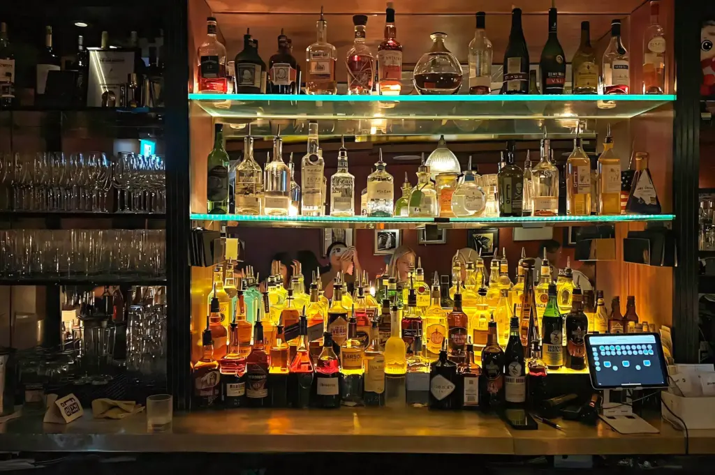 Straight-on close-up shot of a well-stocked back bar in Singapore, featuring rows of premium liquor bottles and glassware under warm accent lighting.