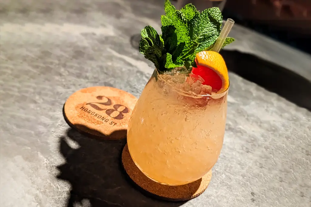Close‑up shot of a refreshing cocktail garnished with mint and citrus, served on a coaster marked “28 HongKong Street” atop a marble bar counter.