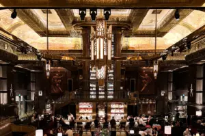 Eye‑level wide‑angle shot of Atlas Bar Singapore showcasing its grand Art Deco interior, towering backlit gin shelves, ornate gold detailing, and guests seated across the main bar and dining area.