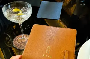 Slightly overhead close‑up of an Atlas Martini with lemon twist beside an Atlas menu on a dark restaurant table, capturing a quiet reflection on what good dish means.