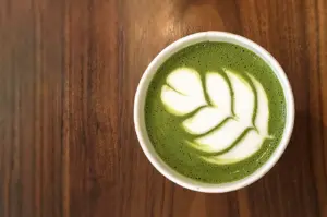 Overhead flat lay shot of a creamy matcha latte with latte art in a white cup on a wooden table, showcasing high-quality ceremonial grade matcha in Singapore brunch culture