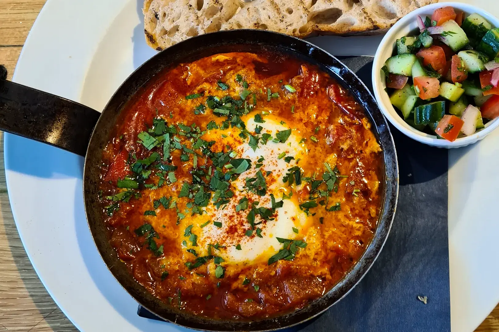 Top-down overhead shot of Tunisian shakshuka at Wild Honey Singapore, cast iron pan with baked eggs in rich tomato sauce, herbs, bread and side salad, popular brunch dish Orchard Road