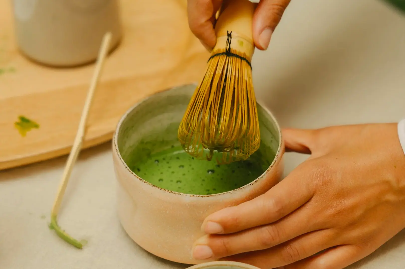 Close-up angle of a bamboo whisk mixing ceremonial grade matcha powder in a ceramic bowl, demonstrating traditional Japanese matcha preparation technique