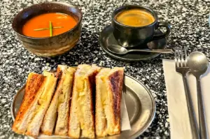 ye-level cafe shot of grilled cheese sandwich with melted cheese, tomato soup, and black coffee on marble table – classic comfort food meal for emotional eating