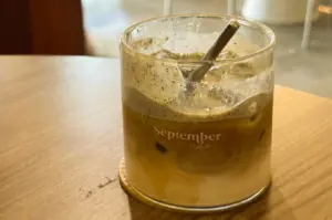 Close-up eye-level shot of an iced black sesame latte in a glass at September Coffee, minimalist viral café with layered drink styled for Instagram photography