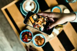 Smartphone capturing Instagram worthy Singapore food with colorful dishes and sauces on wooden table, photographed in close overhead angle showing food photography setup