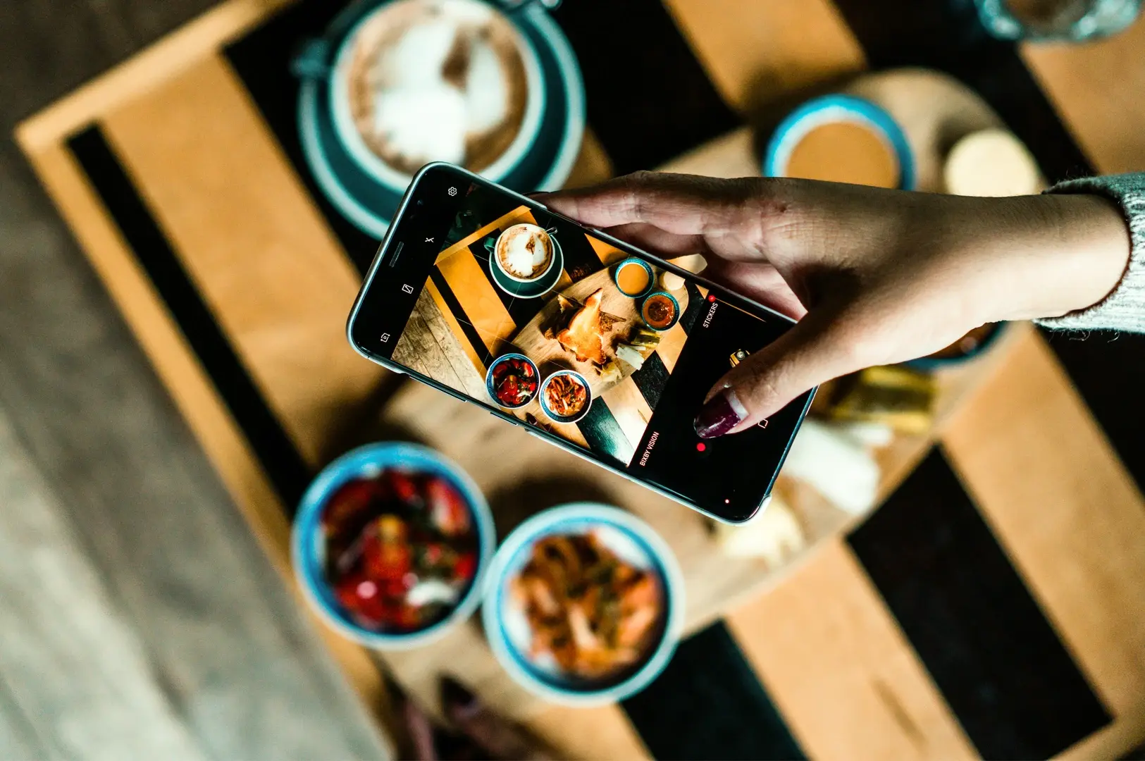 Smartphone capturing Instagram worthy Singapore food with colorful dishes and sauces on wooden table, photographed in close overhead angle showing food photography setup