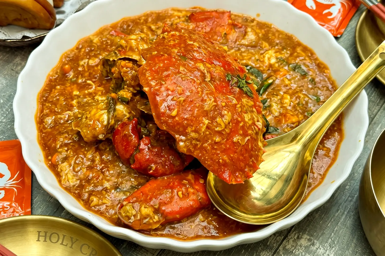Singapore chili crab in rich spicy sauce with whole crab and herbs in white bowl, close-up hero shot at Instagrammable seafood restaurant