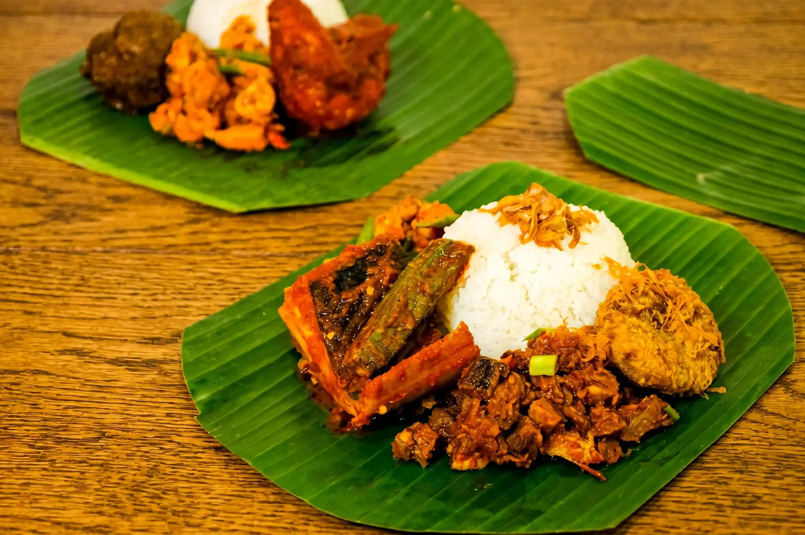 Banana leaf rice with assorted Malay curries, fried chicken, vegetables, and sambal served on green leaf at an Instagram worthy restaurant in Singapore, angled top-down food photography