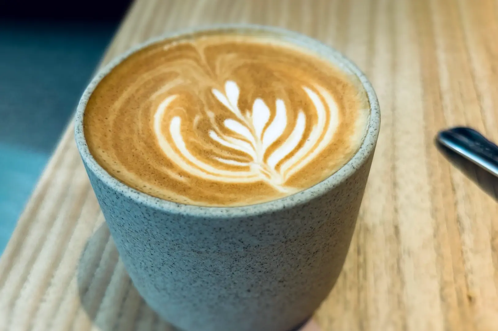 Top-down close-up shot of latte art coffee in ceramic cup at Lola’s Cafe Kovan, featuring freshly ground espresso with creamy milk foam – signature brunch drink in Singapore cafes