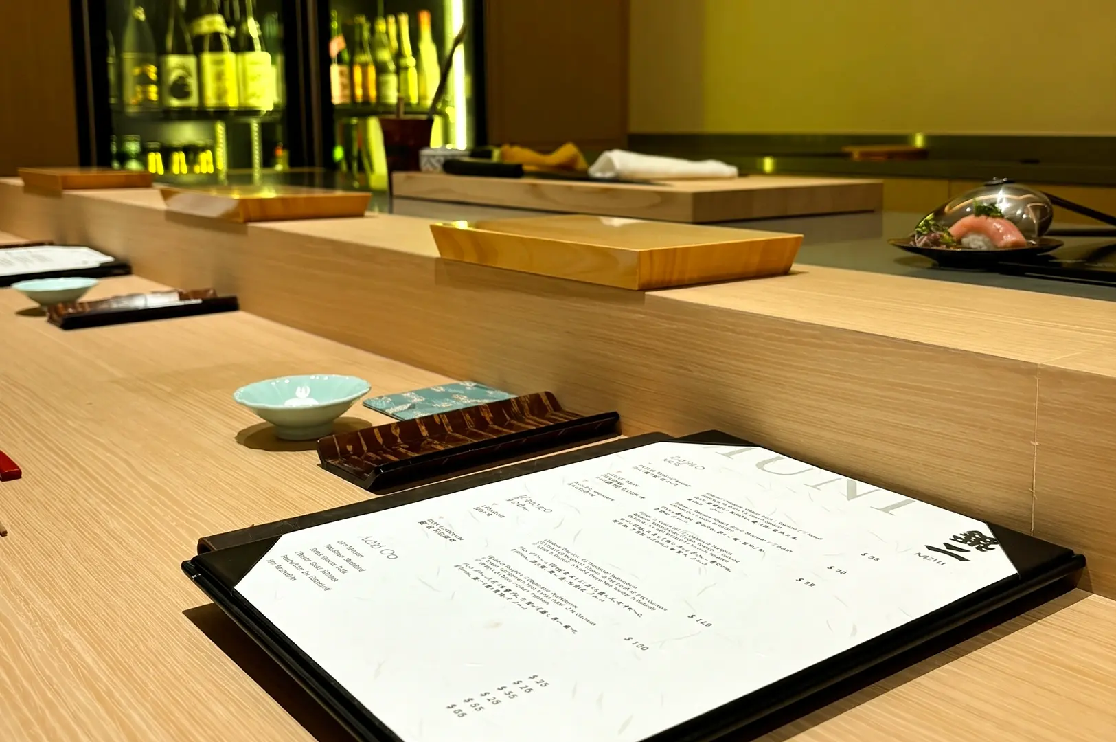 Angled close-up shot of omakase counter menu at Sushi Muni Singapore, showcasing wooden sushi bar setup and Japanese fine dining ambiance
