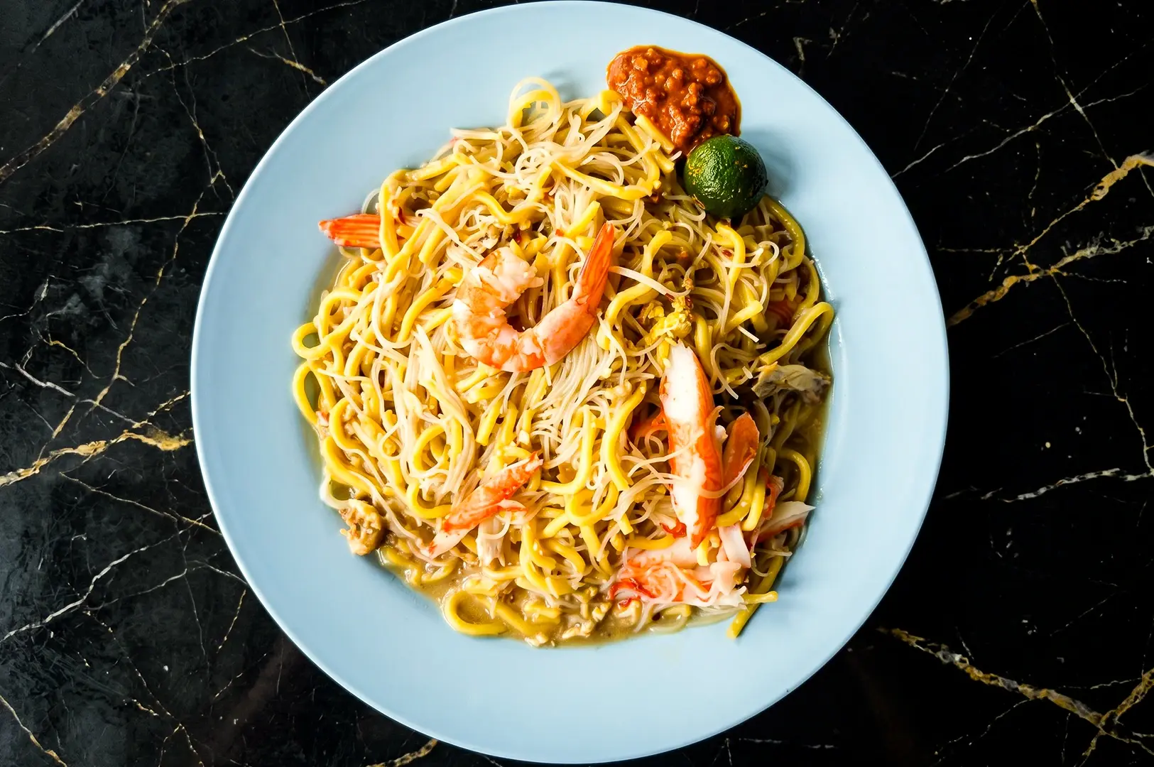 Singapore Hokkien mee with yellow noodles, rice noodles, prawns, and sambal chili served on plate, captured in top-down flat lay food photography