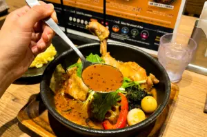 Close-up eye-level food photography of Sapporo chicken soup curry at Soup Curry GARAKU, featuring a spoonful of spiced broth, roasted vegetables, quail eggs and tender chicken in a traditional Japanese comfort food bowl.