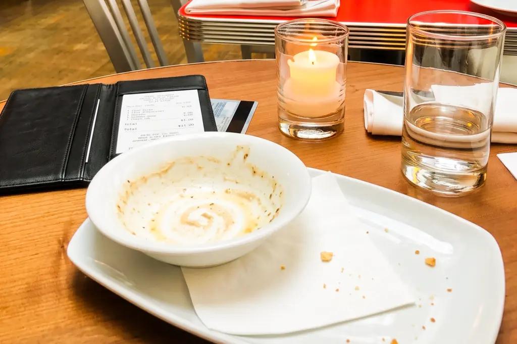 Eye-level close-up of a restaurant table after a shared meal, featuring an empty bowl, dining receipt, candle, water glass, and bill holder, illustrating bill splitting, dining etiquette, group dining expenses, and social dining culture in Singapore.
