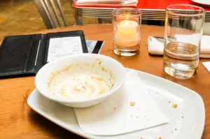 Eye-level close-up of a restaurant table after a shared meal, featuring an empty bowl, dining receipt, candle, water glass, and bill holder, illustrating bill splitting, dining etiquette, group dining expenses, and social dining culture in Singapore.
