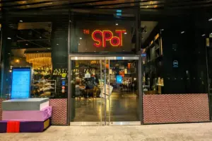 Front-facing eye-level view of The Spot Singapore restaurant entrance at Marina One with neon signage and modern glass facade at night