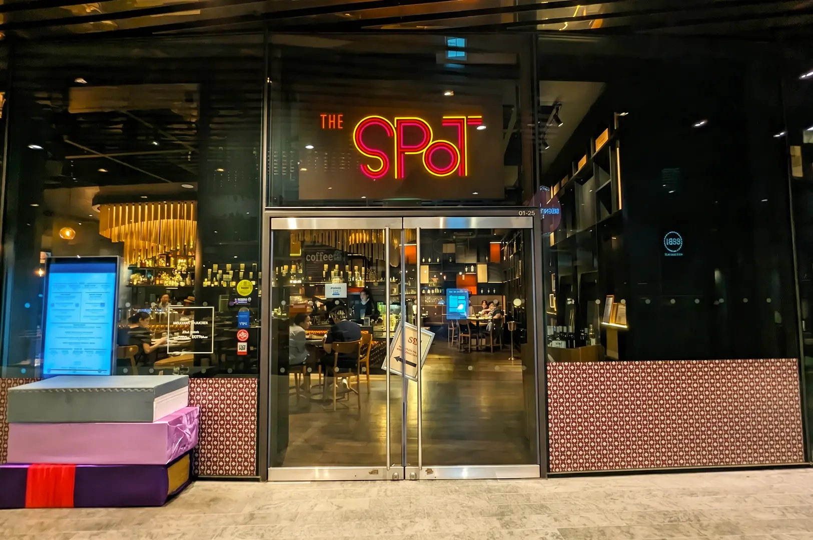 Front-facing eye-level view of The Spot Singapore restaurant entrance at Marina One with neon signage and modern glass facade at night