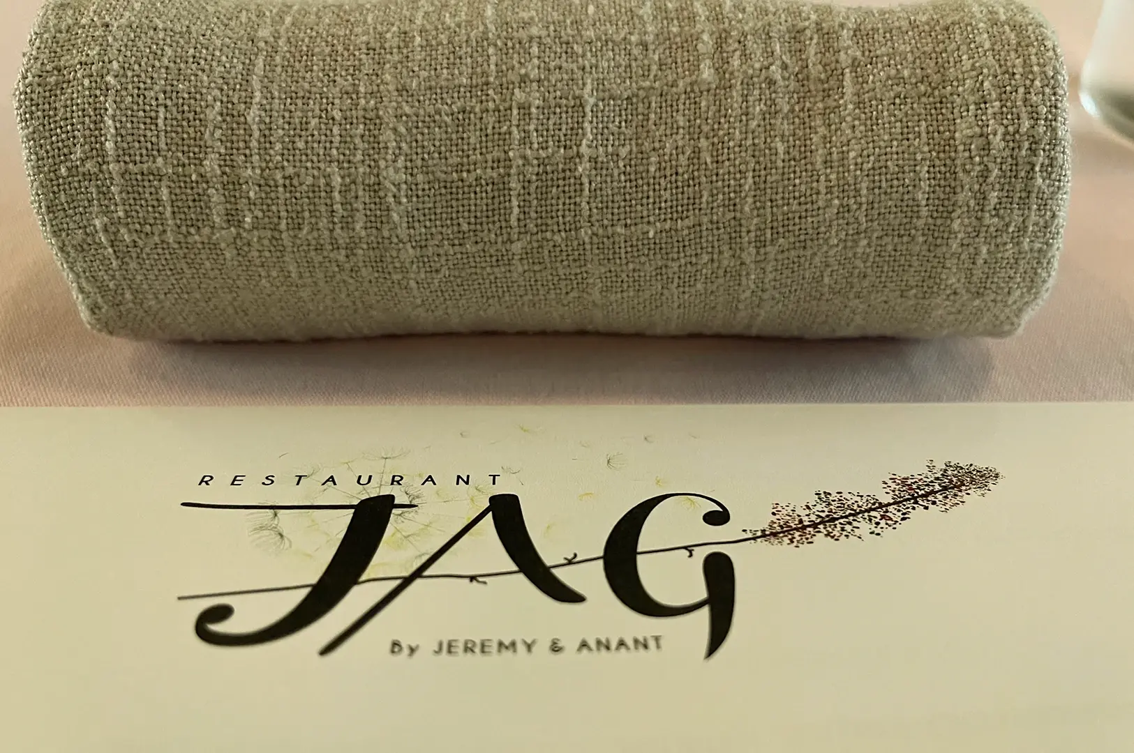 Top-down close-up shot of Restaurant JAG menu with elegant logo and folded napkin, representing a Michelin-starred French fine dining experience in Singapore focused on refined presentation