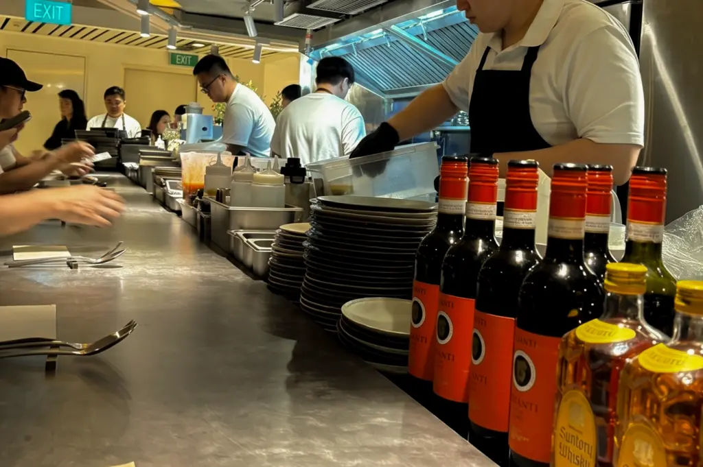 Eye-level counter-side view of Sio Pasta Singapore's open kitchen at Raffles City, showcasing chefs preparing Japanese-style handmade pasta while diners enjoy the intimate 28-seat restaurant experience.