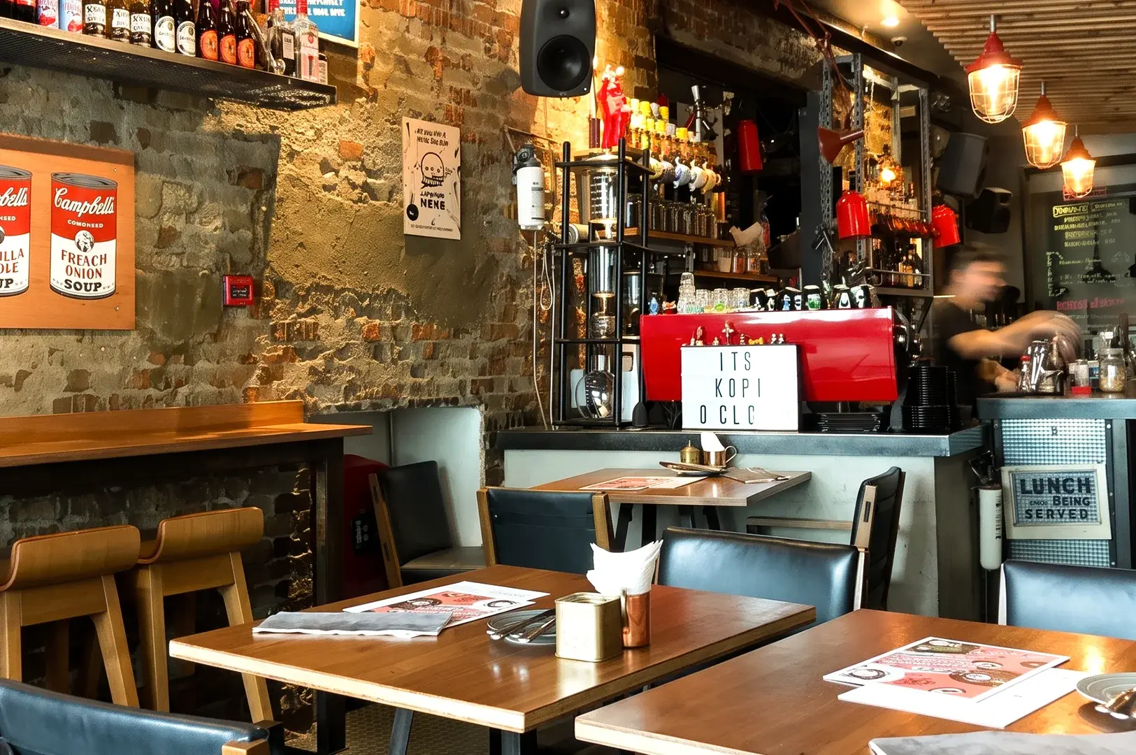 Wide-angle interior shot of Symmetry Cafe at 9 Jalan Kubor in Singapore, featuring rustic brick walls, cozy dining tables, coffee bar, and all-day brunch dining atmosphere near Bugis MRT Station.